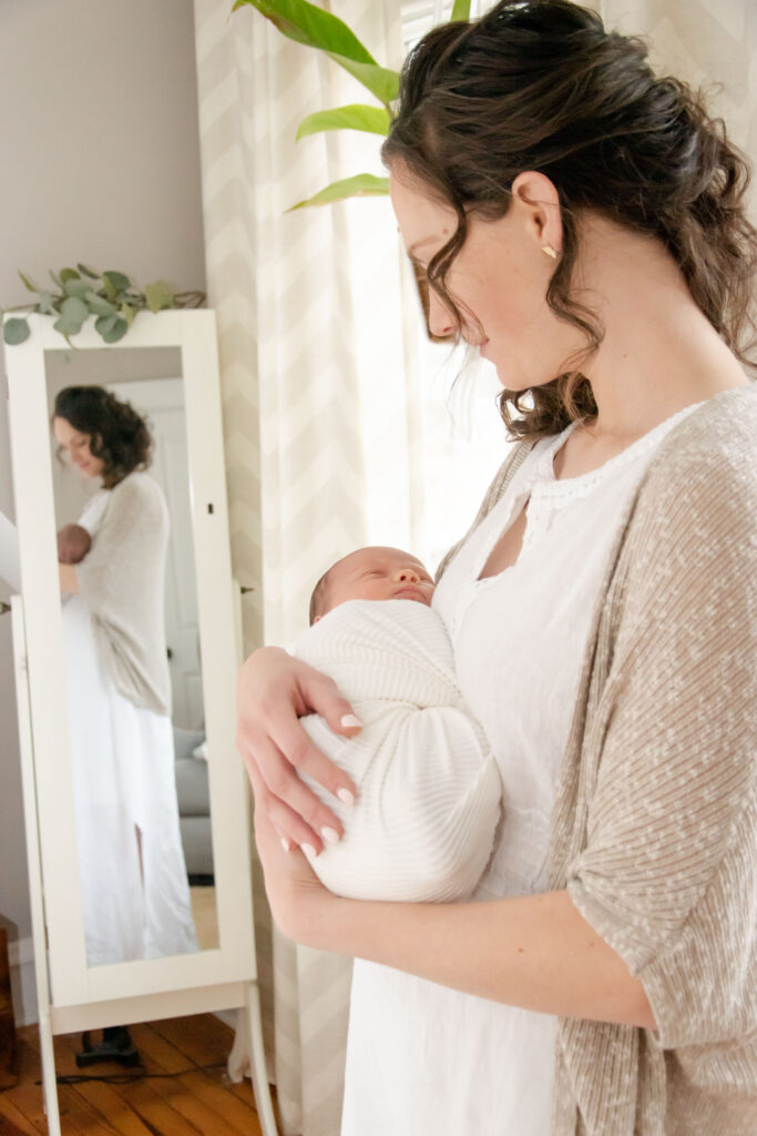 Mom standing in a mirror with newborn baby.