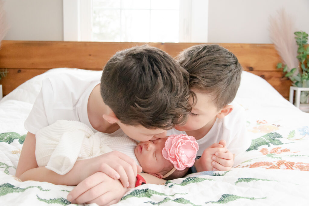 two brothers giving their baby sister a kiss.