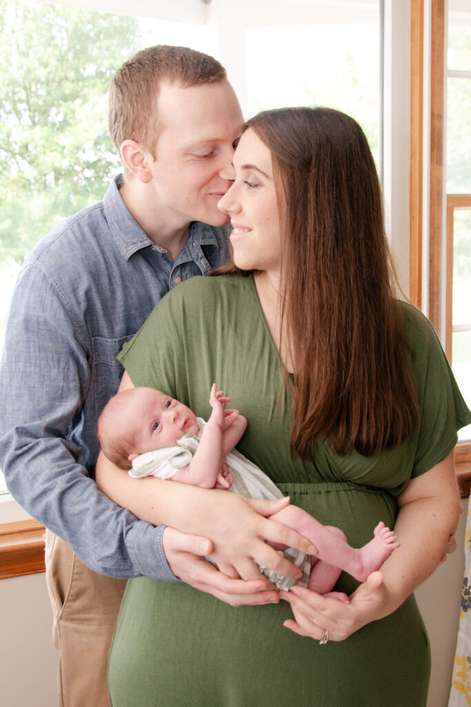 Mom in green dress and dad in blue shirt. They are holding their newborn baby. Landon Lifestyle Newborn session.