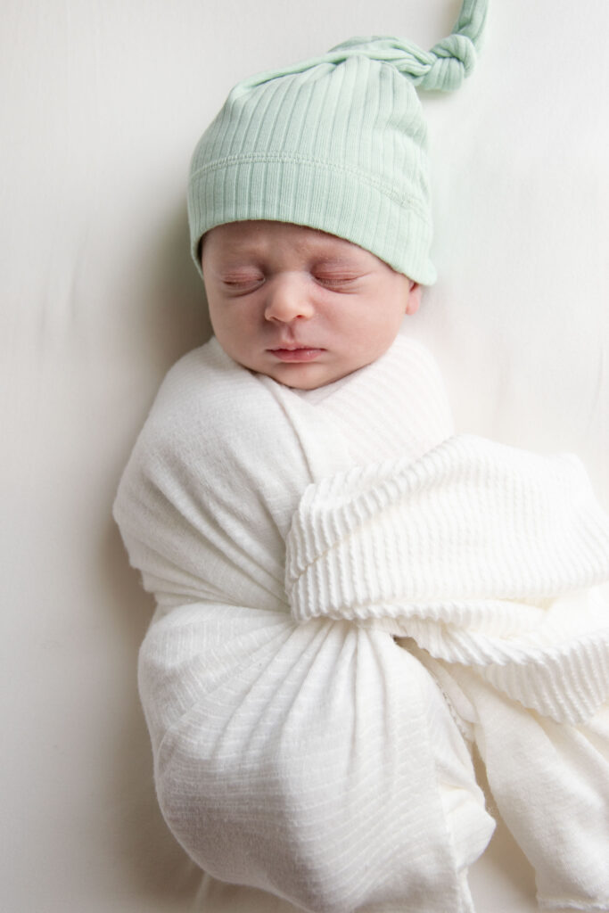 Landon Lifestyle Newborn session. Newborn sleeping in teal hat. The baby is wrapped in a white swaddle.