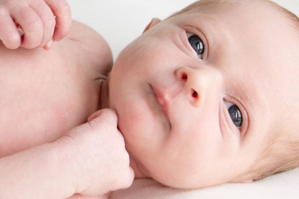 Newborn baby with their eyes open looking at the camera. The baby has blue eyes. Landon Lifestyle Newborn session.