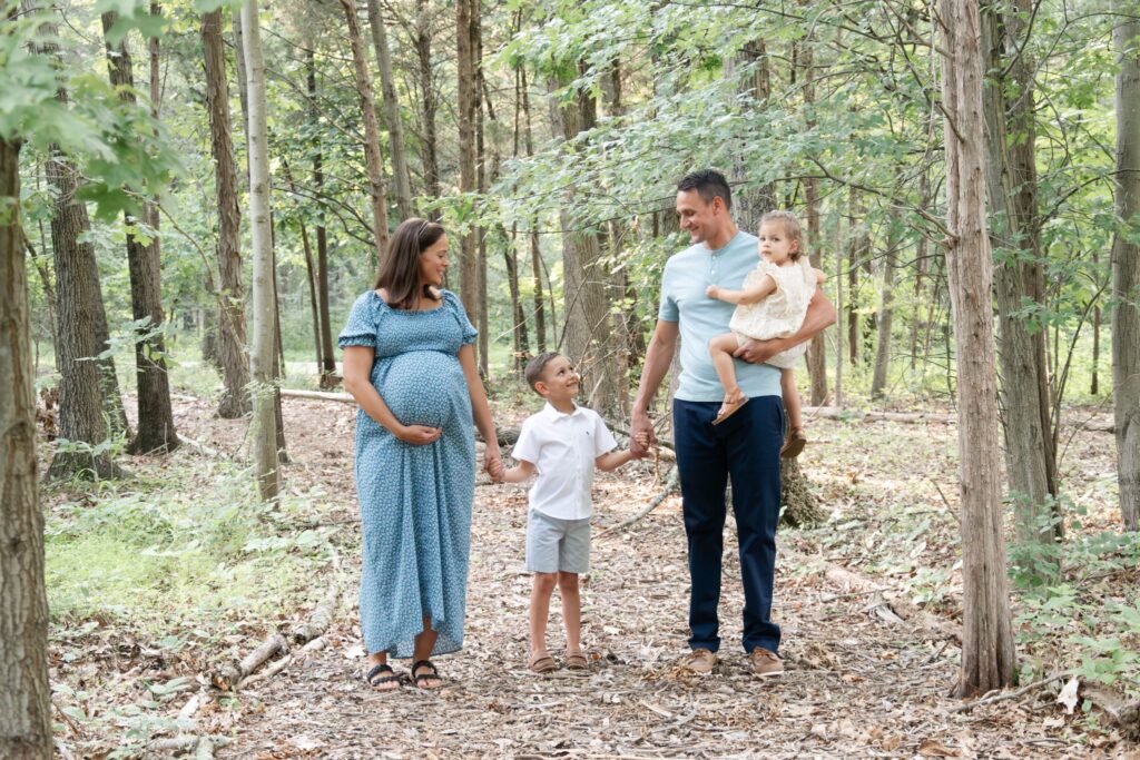 Family in woods holding hands and looking at each other.