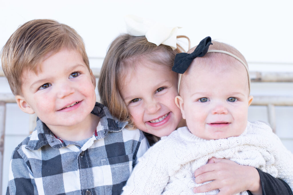 Three siblings sitting on a bench smiling.