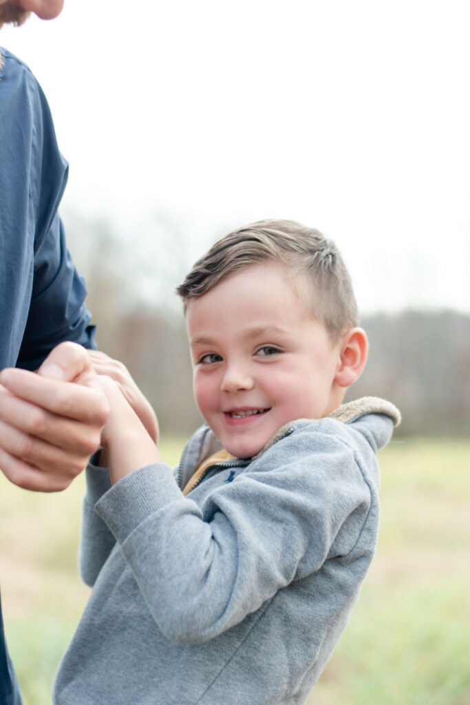 Little boy holding himself up on dads arm.