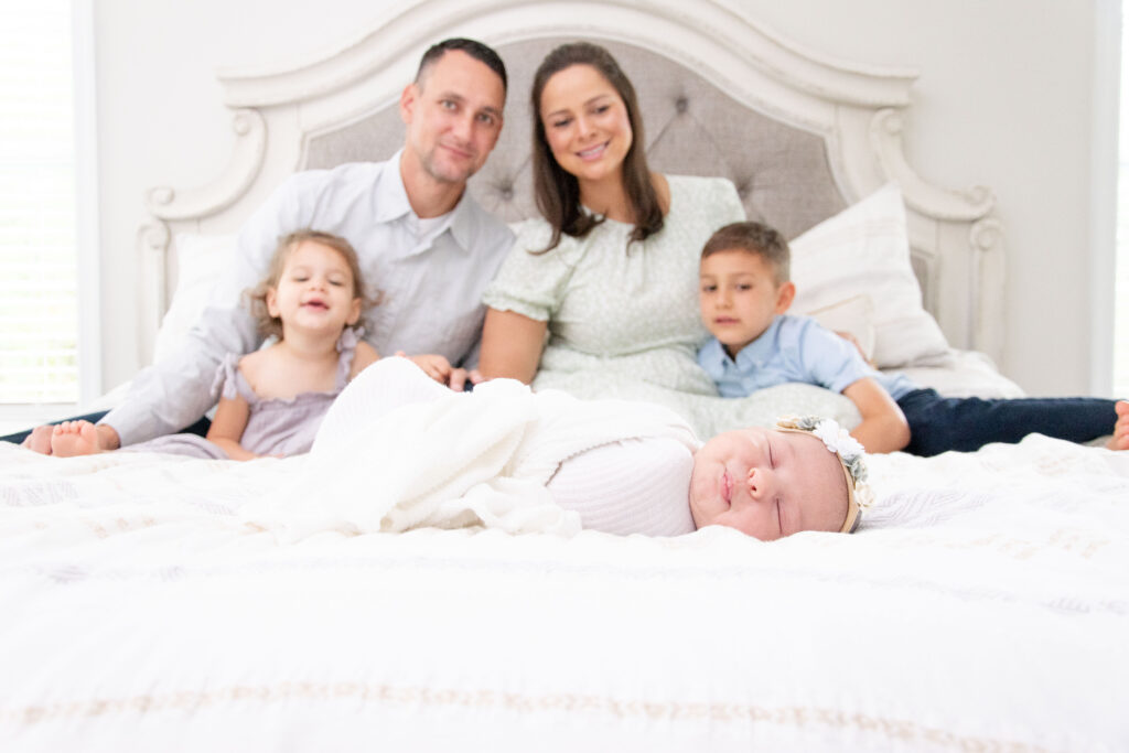 Family sitting on bed with new baby and siblings. Adjust to a New Sibling. 