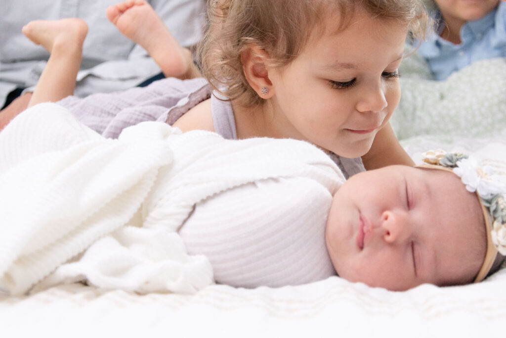 Toddler laying down holding newborn sister.