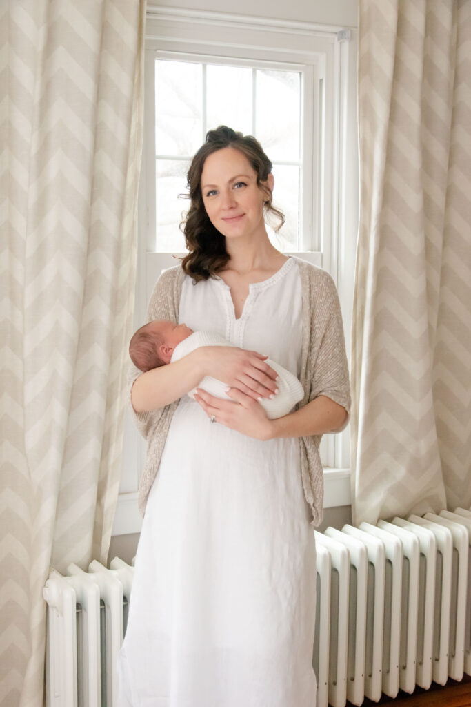 Mom in a white dress swaddled in a white blanket, holding a newborn baby. 