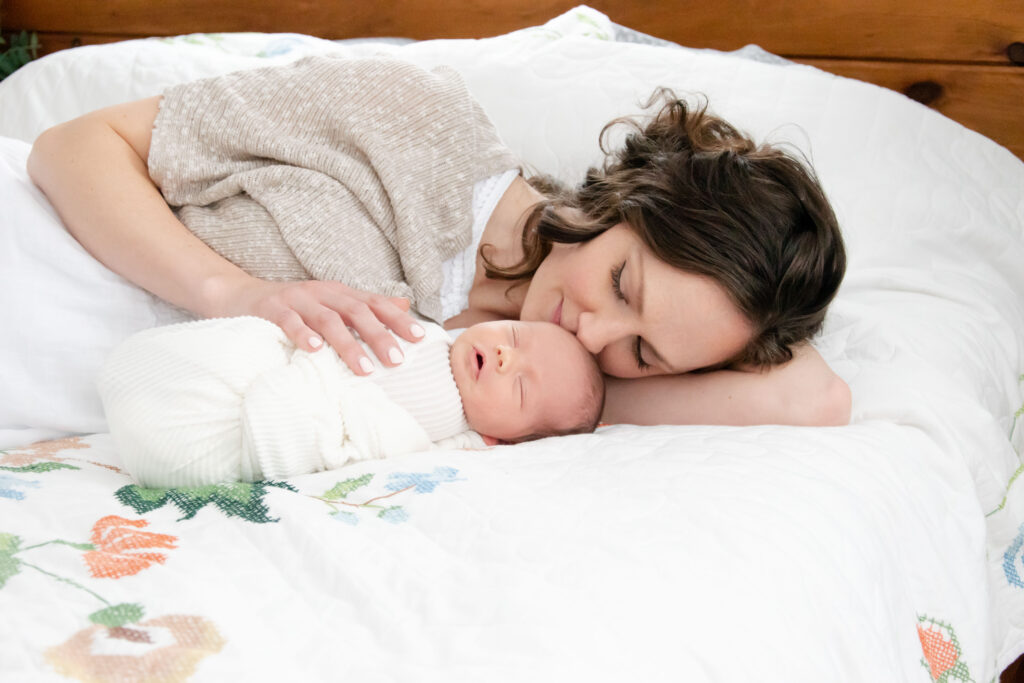 Mom with newborn on bed with a white comforter. In-home photography.