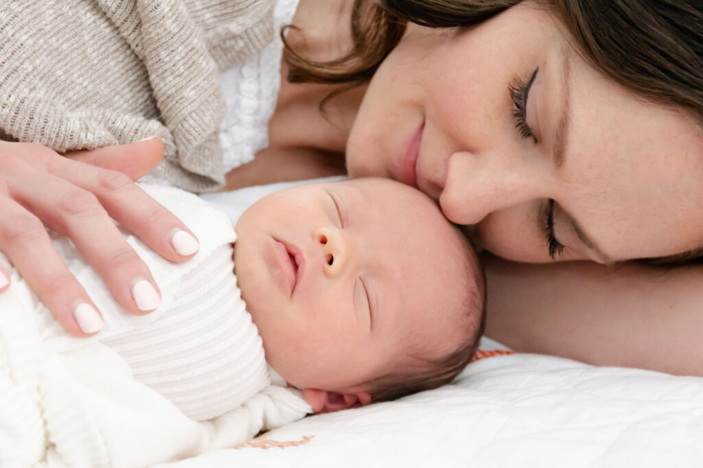 Newborn baby with mom snuggling. Baby is swaddled in a white blanket.In-home newborn photography.