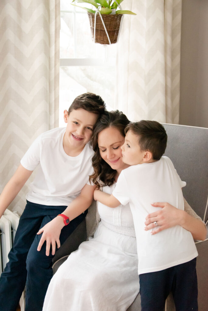 Mom with two sons. Sittin on a gray chair hugging. In-home newborn photography.