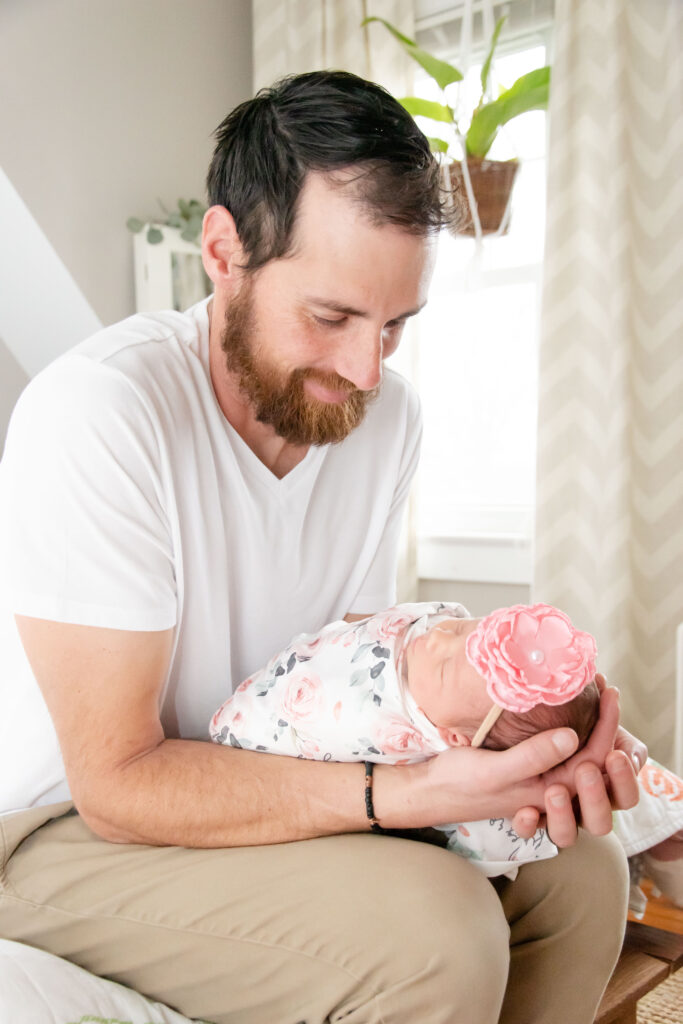 Dad with newborn sitting on the end of the bed. In-home newborn photo.