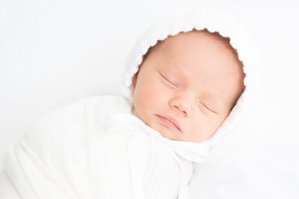 Newborn baby sleeping with a white bonnet. Newborn photography.