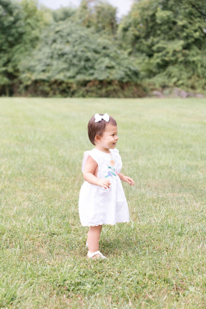 Toddler looking in the distance laughing wearing a white dress.