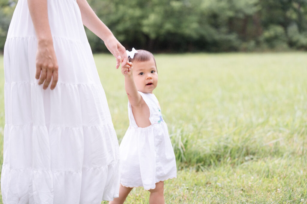 Toddler holding a hand walking along in a green field.