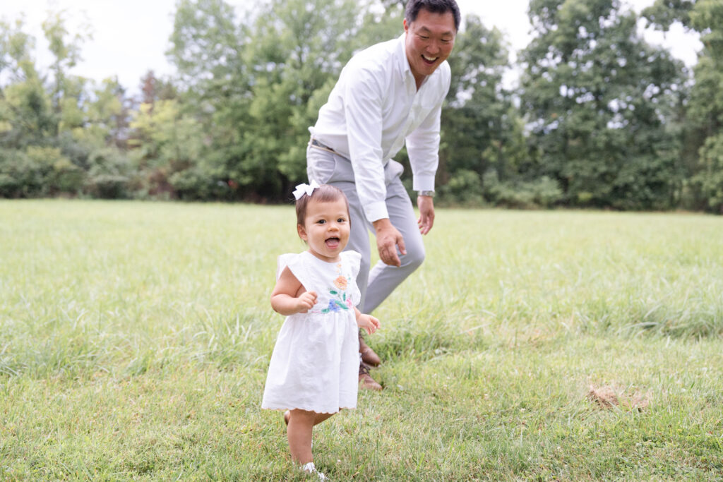 Toddler looking and smiling as dad chases her.