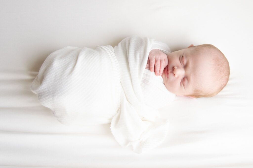 newborn baby wrapped in a white swaddle sleeping peacefully. 