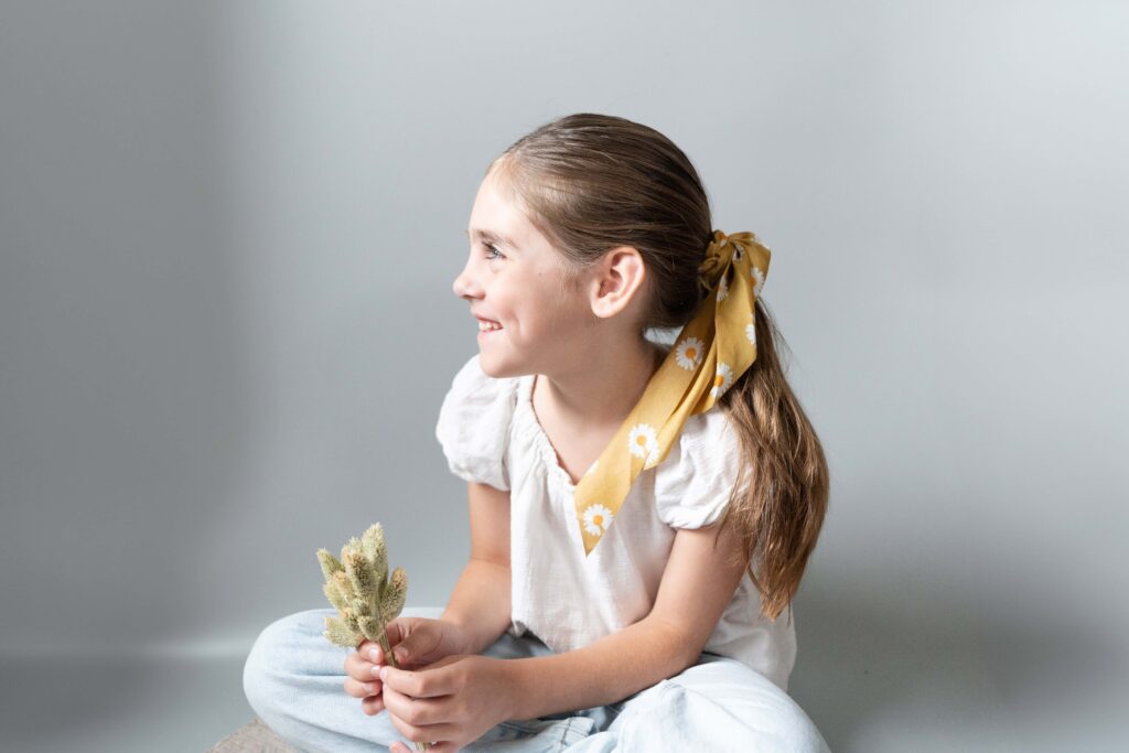 Young girl with a yellow hair tie looking off to the side wearing white for her brand shoot.
