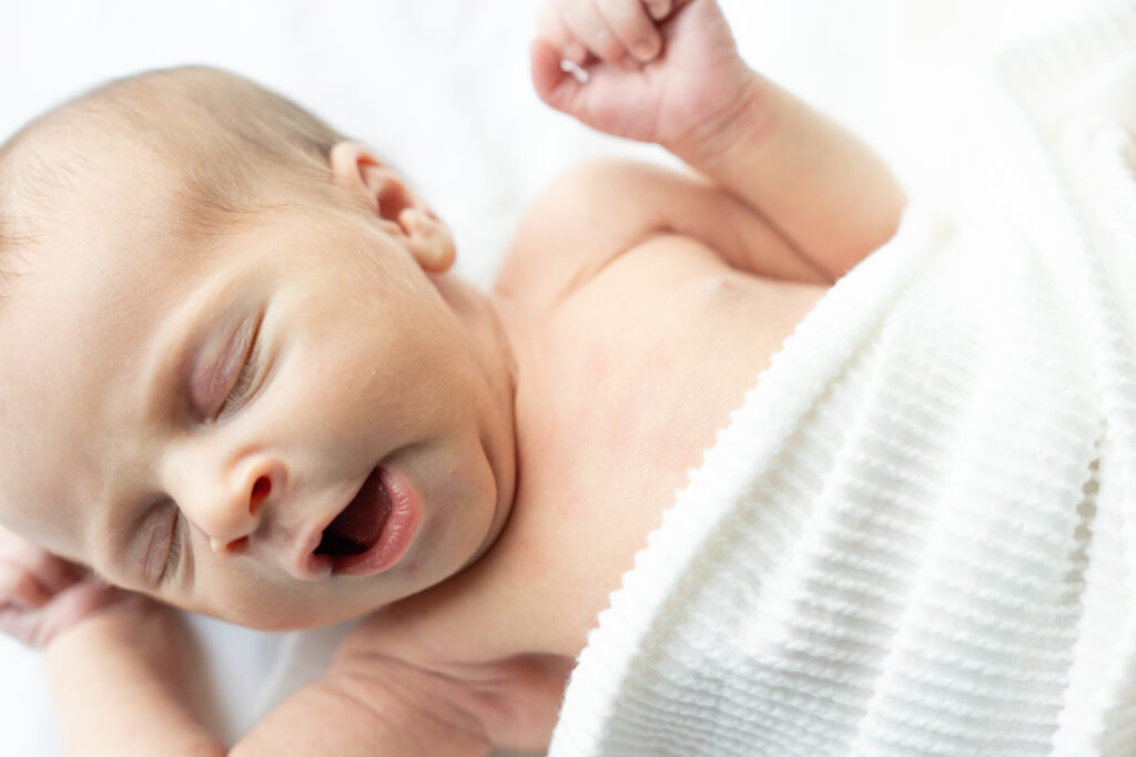 Newborn baby in white swaddle getting ready to stretch.