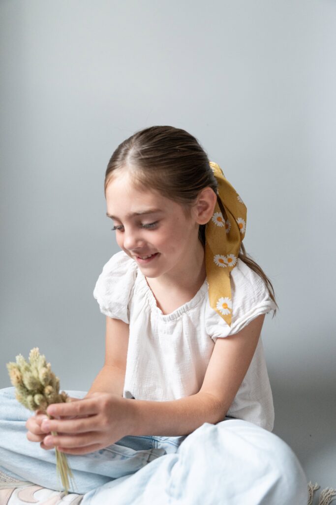 Girl sitting holding flowers with a yellow hair scrunchie in her hair.